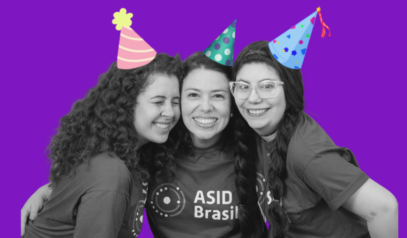 Três mulheres da equipe da ASID se abraçando e vestindo chapeuzinhos de festa.